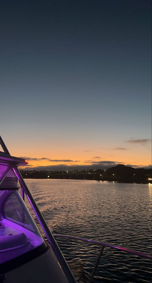 a boat is sitting in the water at night with purple lights on it's side