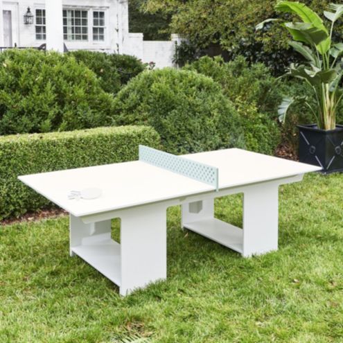 a ping pong table sitting in the middle of a lawn next to some bushes