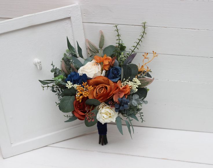 a bridal bouquet with orange, white and blue flowers on the side of a door