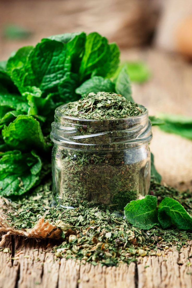 a jar filled with green herbs sitting on top of a wooden table next to leaves