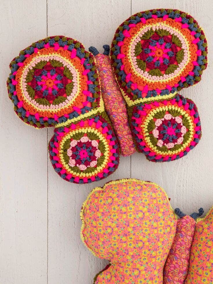 two crocheted pillows and an elephant pillow on a white wooden floor with pink, green, blue, yellow and red colors