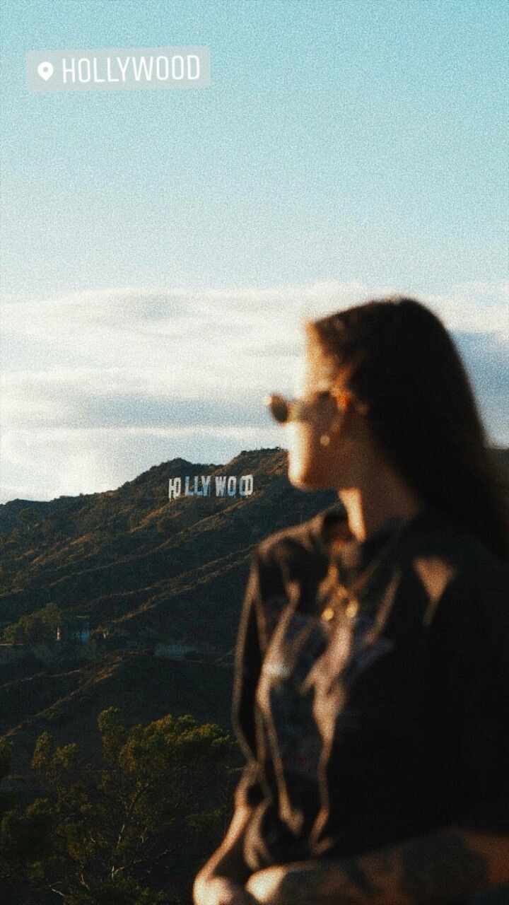 a woman standing on top of a hill looking at the sky and hills behind her