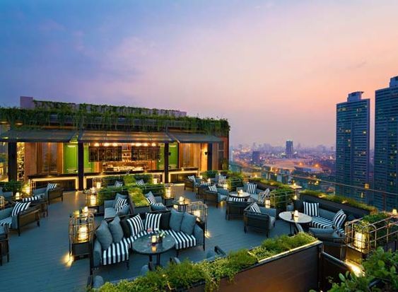 an outdoor restaurant with lots of tables and chairs on top of a roof in the city