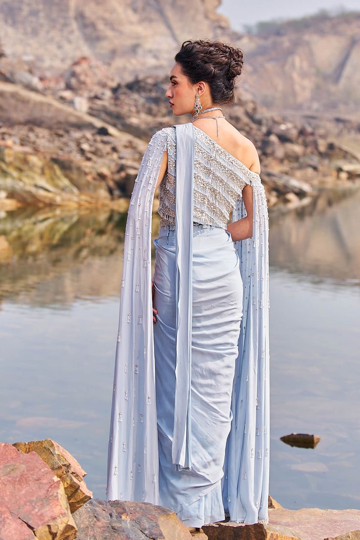 Make a splash in this refreshing aqua drape embellished sari crafted from crepe, paired with a stunning cape one-shoulder blouse. Intricately handcrafted with crystal drops, the padded blouse ensures a comfortable fit with its back hook closure, adding an extra touch of elegance to your ensemble. Traditional Draped Sleeve Georgette Gown, Festive Occasion Wear Pre-draped Saree, Party Pre-draped Saree With Cape Sleeves, Festive Pre-draped Traditional Saree, One Shoulder Fitted Saree, Embellished One-shoulder Evening Saree, Evening One Shoulder Embellished Pre-draped Saree, Evening One-shoulder Embellished Pre-draped Saree, Party Wear Saree With Cape Sleeves