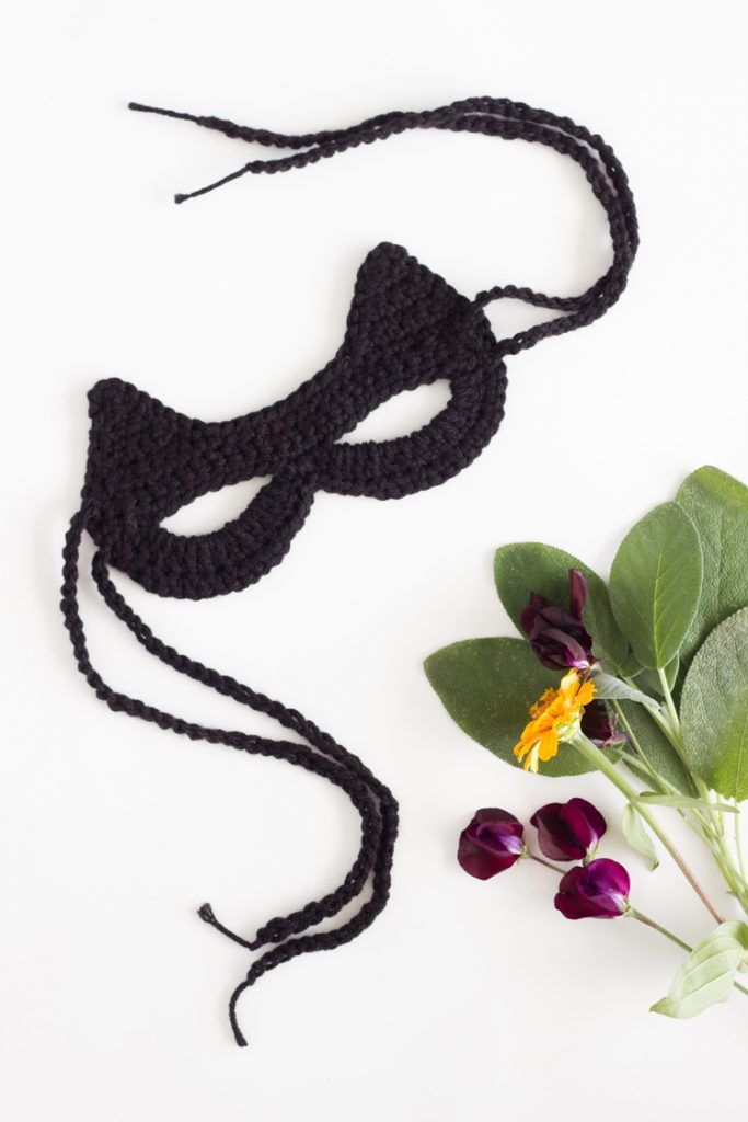 a crocheted mask next to flowers on a white surface