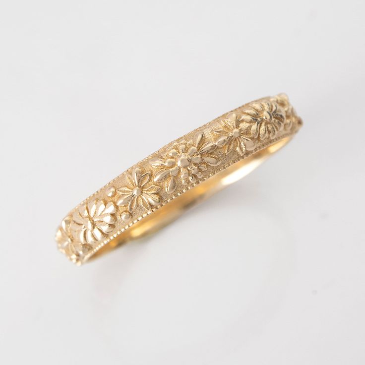 a yellow gold ring with flowers on the inside and outside, sitting on a white surface