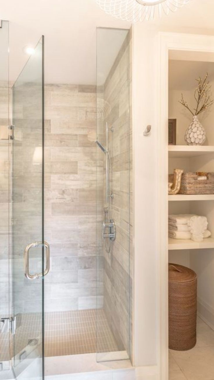 a walk in shower sitting inside of a bathroom next to a shelf filled with towels