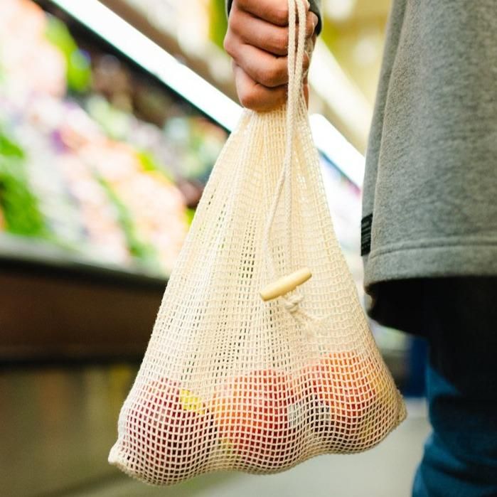 a person holding a mesh bag full of apples in the produce section of a grocery store