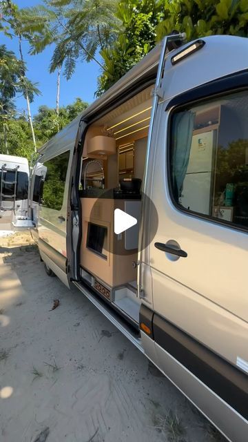 an rv parked on the beach with its door open and another vehicle in the background