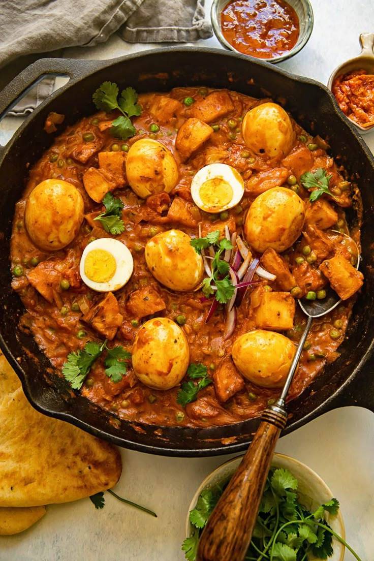 a skillet filled with meat and eggs on top of a table next to bread