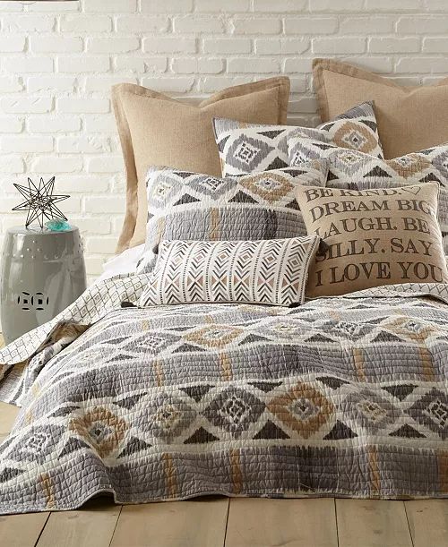 a bed covered in pillows and blankets next to a brick wall