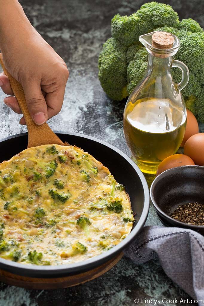 a person is holding a wooden spoon over a skillet with broccoli and eggs