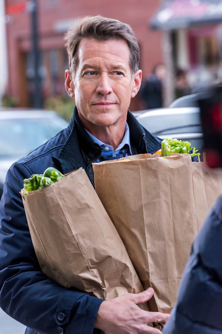 a man holding two brown paper bags with lettuce in it's hands