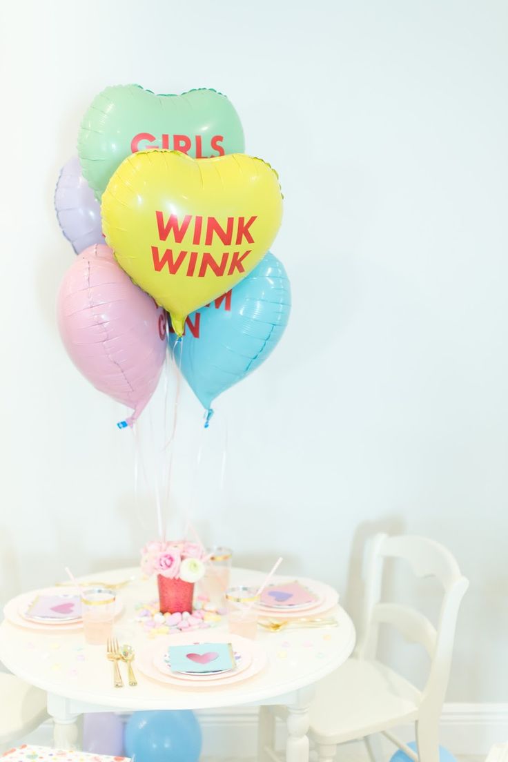 a table topped with balloons and cupcakes next to a wall mounted sign that says girls wink wink