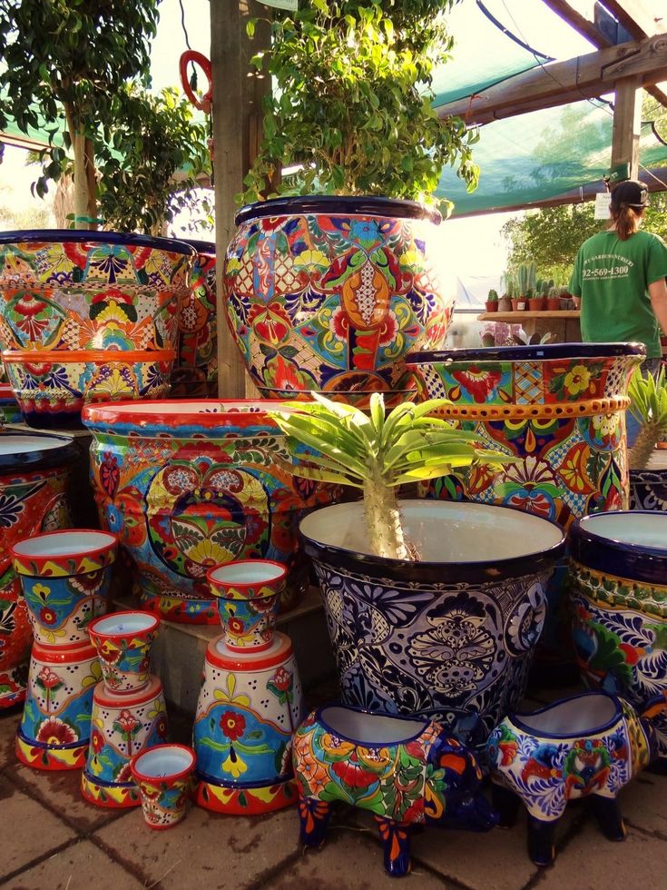 many colorful vases and planters are stacked on the ground in front of a man