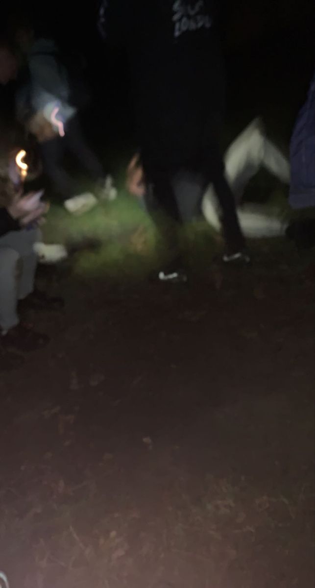 a group of people sitting on the ground at night with one person holding a cell phone