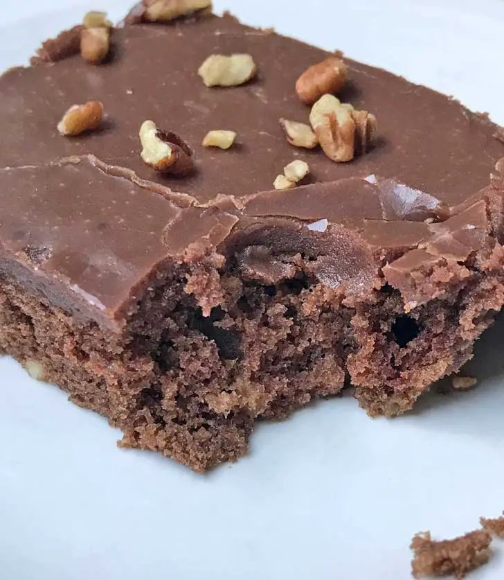 a close up of a piece of cake on a plate with nuts and chocolate frosting