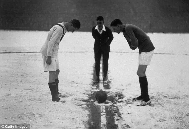 three men are playing soccer in the water with one man looking down at the ball