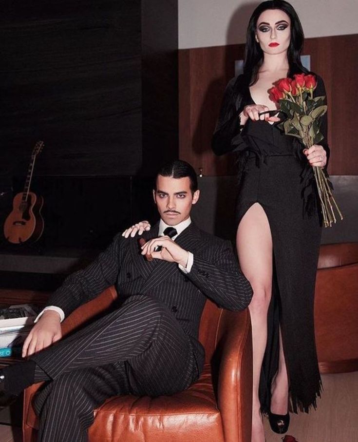 a man sitting on a chair next to a woman in a black dress holding flowers