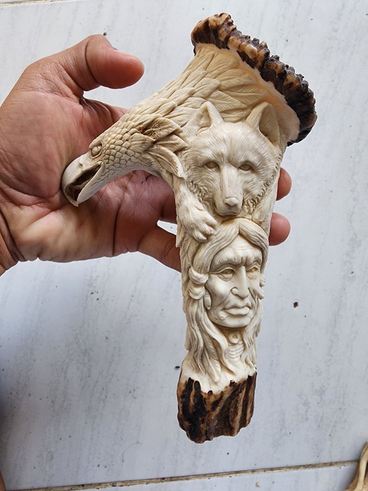 a hand holding a carved animal head on top of a piece of drift wood next to a white marble wall