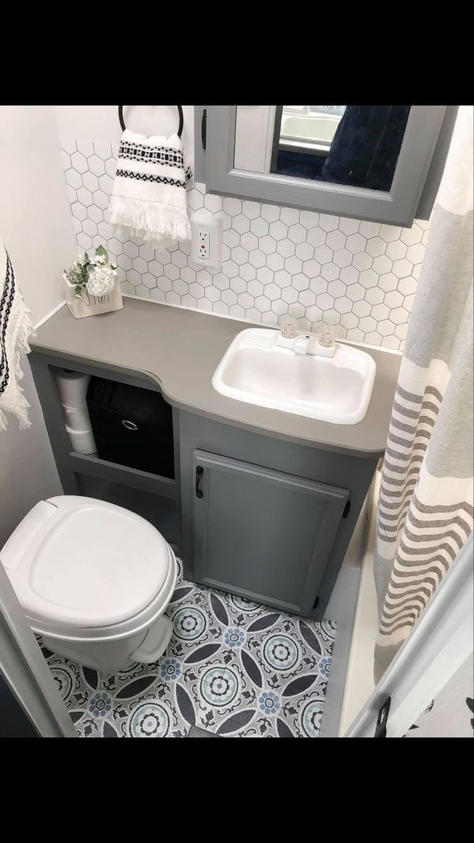 a white toilet sitting next to a sink in a bathroom under a window on top of a tiled floor