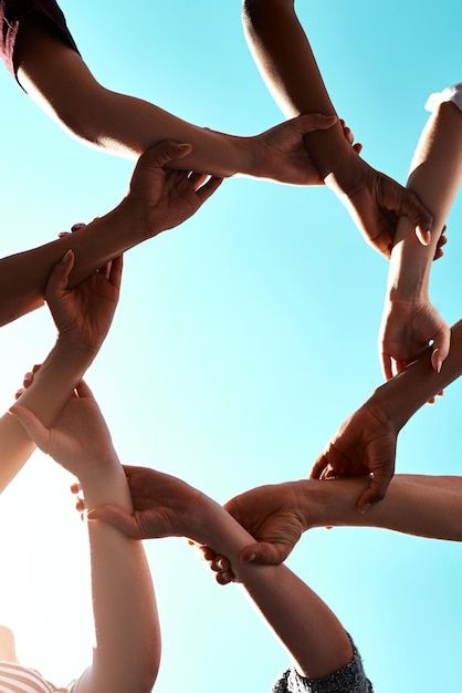 a group of people standing in a circle holding their hands together with the sky behind them