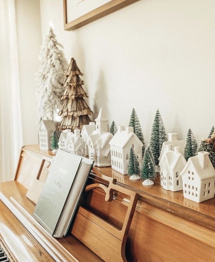 a piano sitting in front of a christmas tree on top of a wooden shelf next to a white house