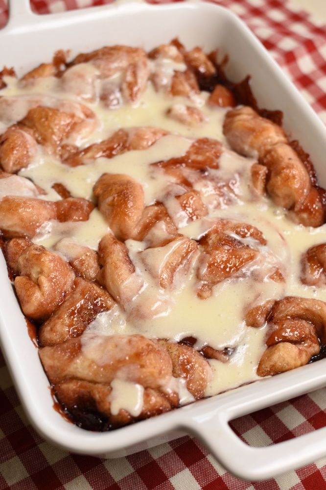 a casserole dish filled with cinnamon rolls covered in white sauce on a red and white checkered tablecloth