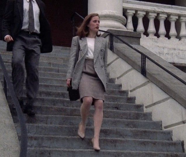 the woman is walking down the stairs with her hand in her pocket and another man behind her