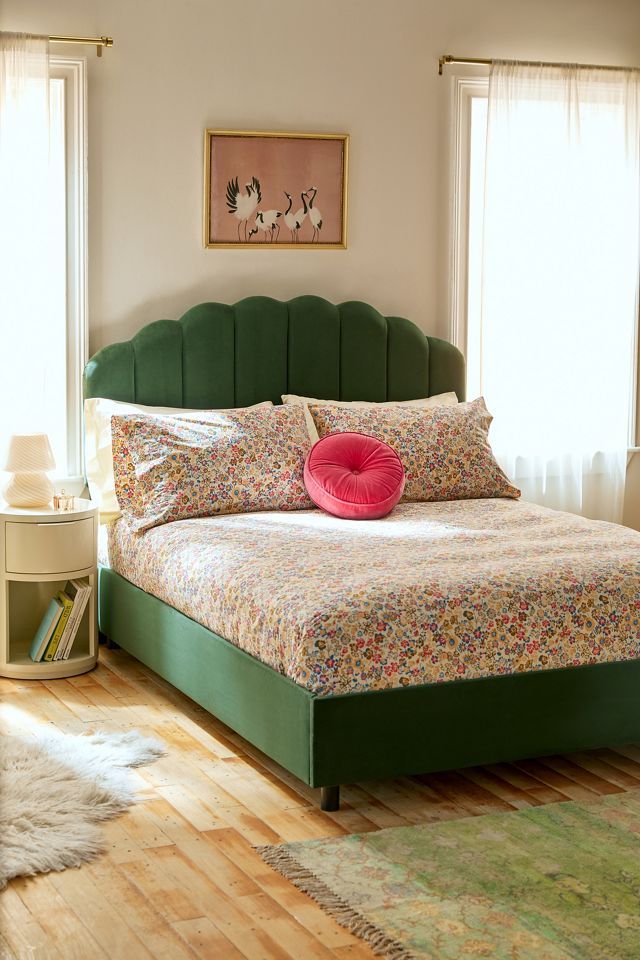 a bed with green headboard and pillows on top of it in a bedroom next to two windows