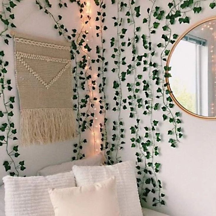 a white bed topped with pillows next to a window covered in green ivy leaves and a round mirror