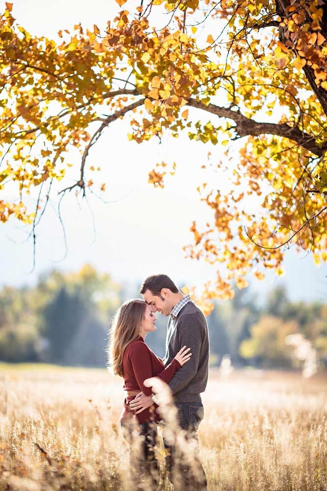 a man and woman standing in tall grass under a tree with their arms around each other