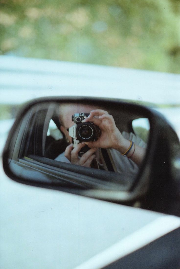 a person taking a photo in the side mirror of a car while holding a camera