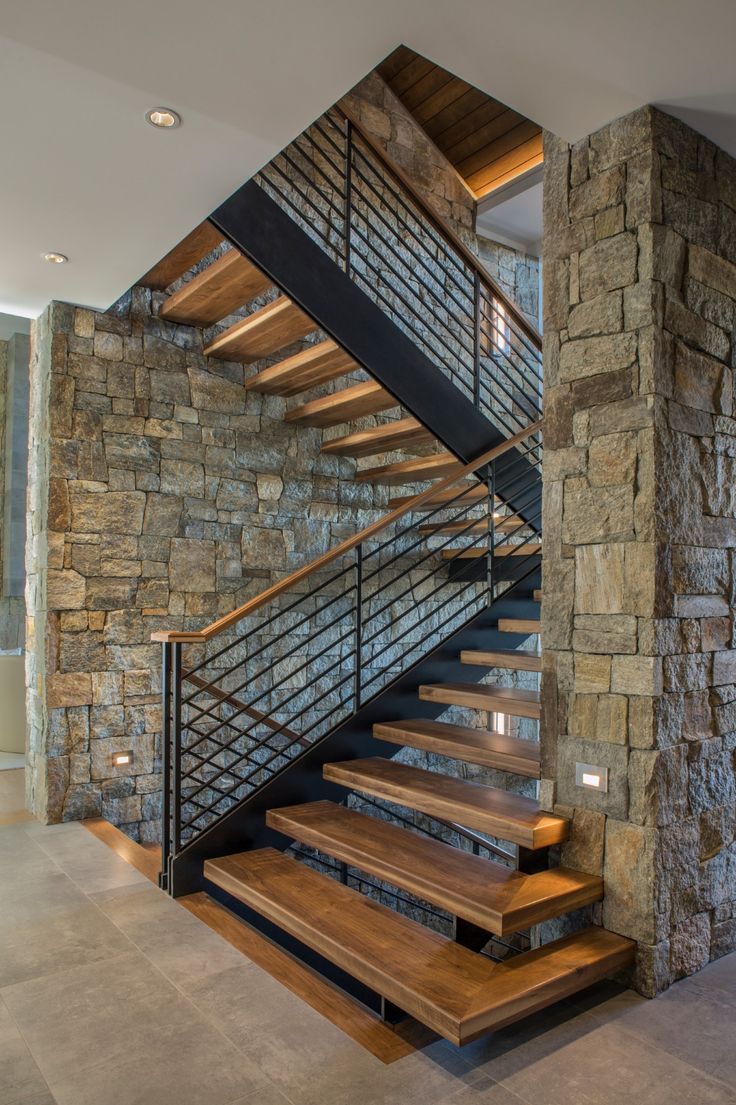 a stone wall and wooden stairs in a modern home with wood steps leading up to the second floor