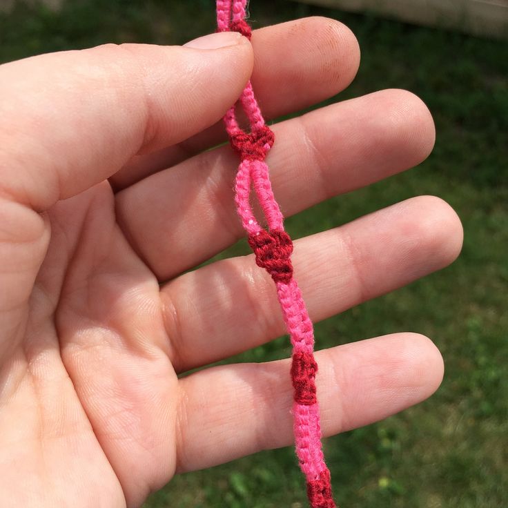 a hand holding a pink string in the palm of it's left hand, with grass in the background