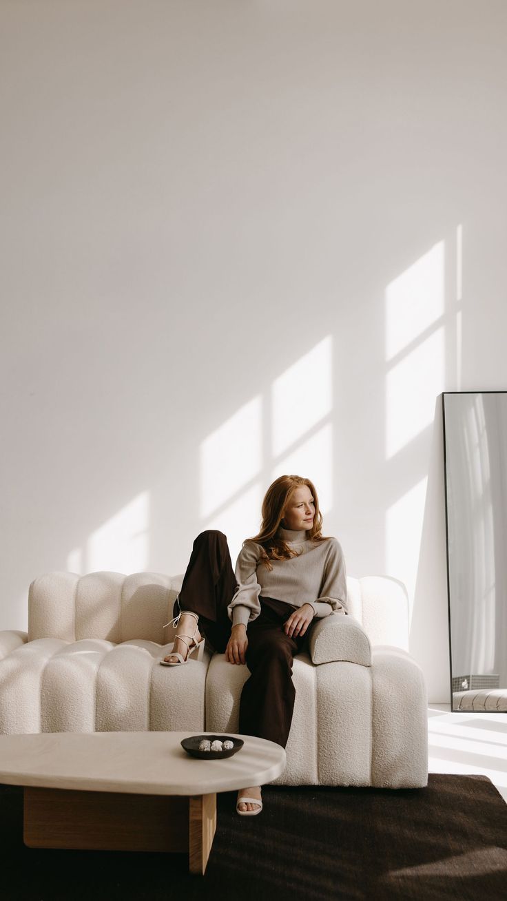 a woman sitting on top of a white couch in a living room next to a coffee table