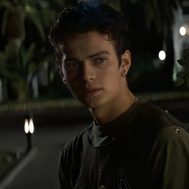 a young man with ear piercings standing in front of a tree at night, looking into the camera