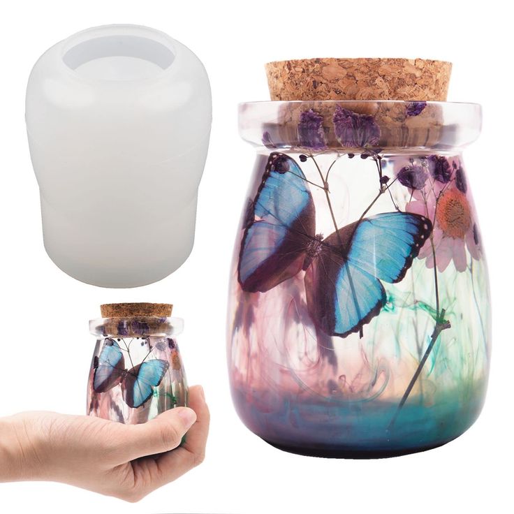 a hand holding a glass jar filled with flowers and butterflies next to a cork lid