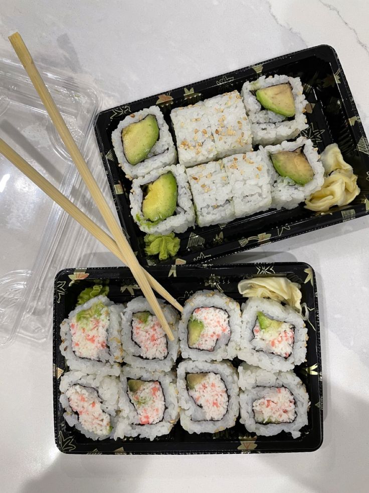 two trays filled with sushi and chopsticks on top of a table