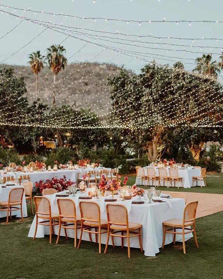 an outdoor dining area with white tablecloths and lights strung over the tables, surrounded by palm trees