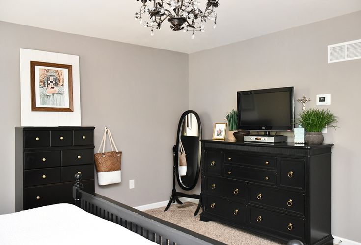 a bedroom with a black dresser, mirror and television on top of it in front of a chandelier