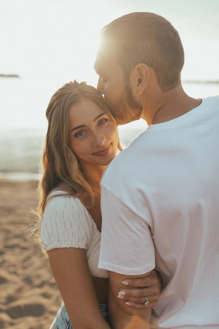 a man and woman standing next to each other at the beach with sun shining on them