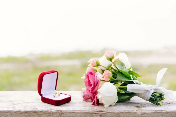 a bouquet of flowers and an engagement ring sitting on a wooden table next to it