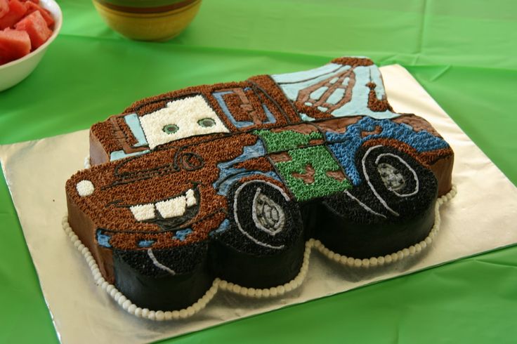 a birthday cake with cars on it and watermelon in the bowl behind it