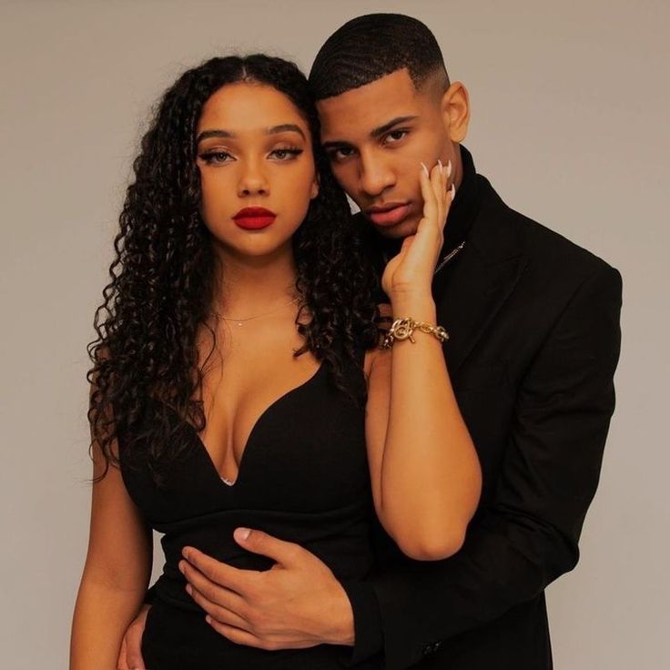 a man and woman standing next to each other in front of a gray background wearing black clothing