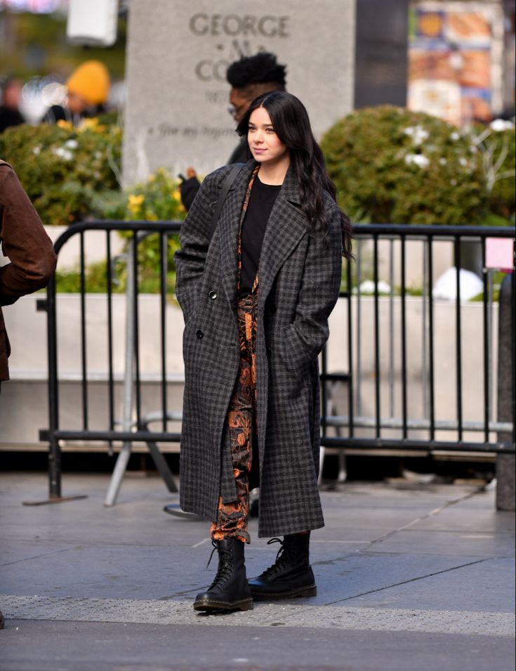 a woman is standing on the sidewalk in front of a fence and looking at something