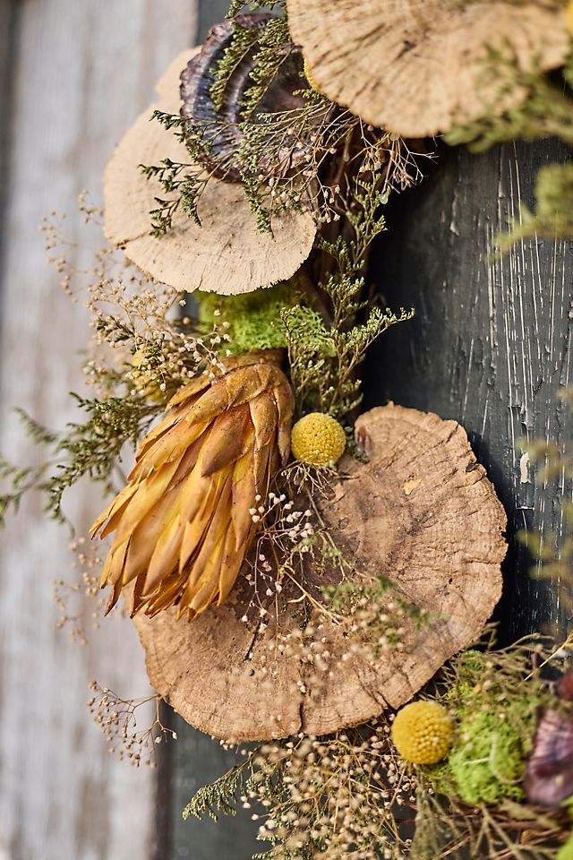 a close up of a wreath made out of tree slices and flowers on a wooden surface