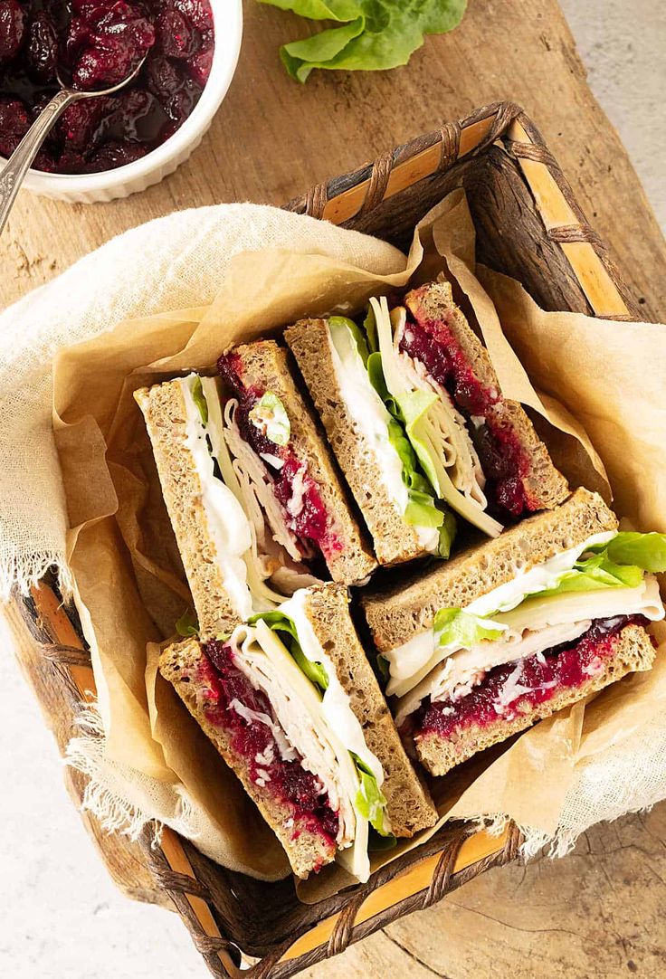 a wooden tray topped with sandwiches and cranberries next to a bowl of cherries