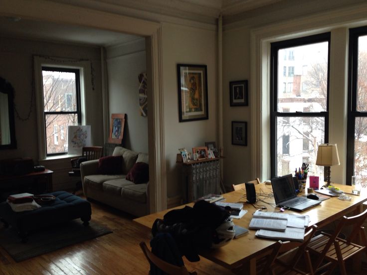 a living room filled with furniture and lots of windows next to a wooden table covered in books