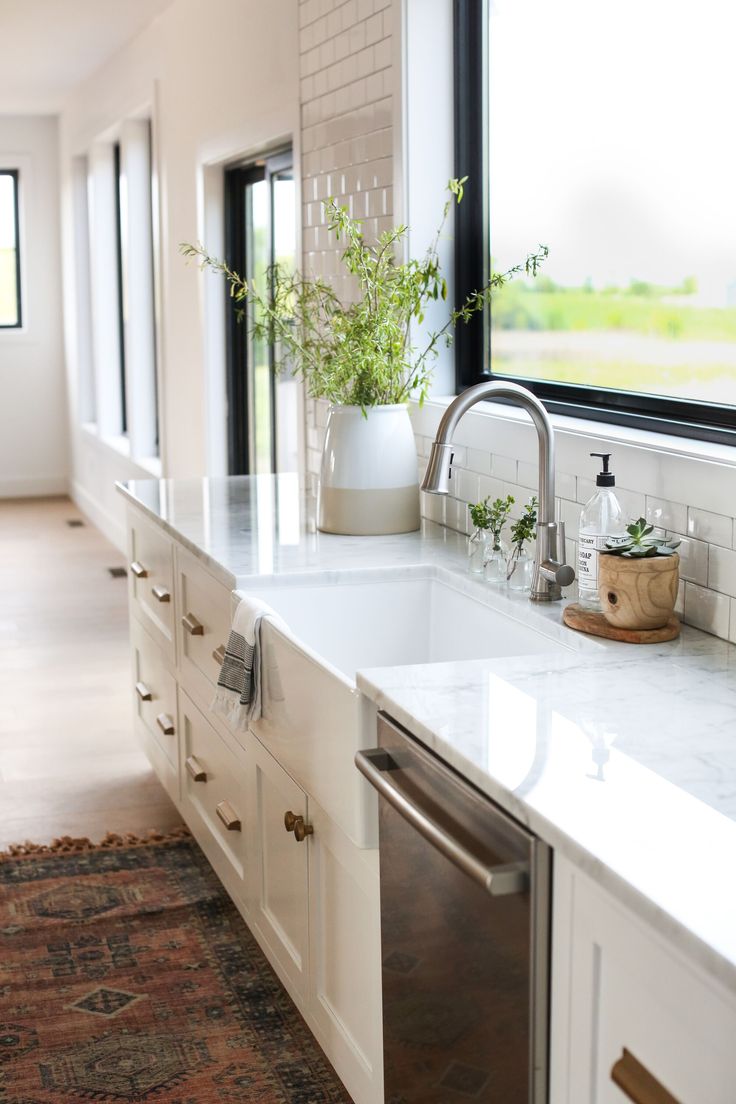 a kitchen with white cabinets and marble counter tops is pictured in this image, there are plants on the window sill